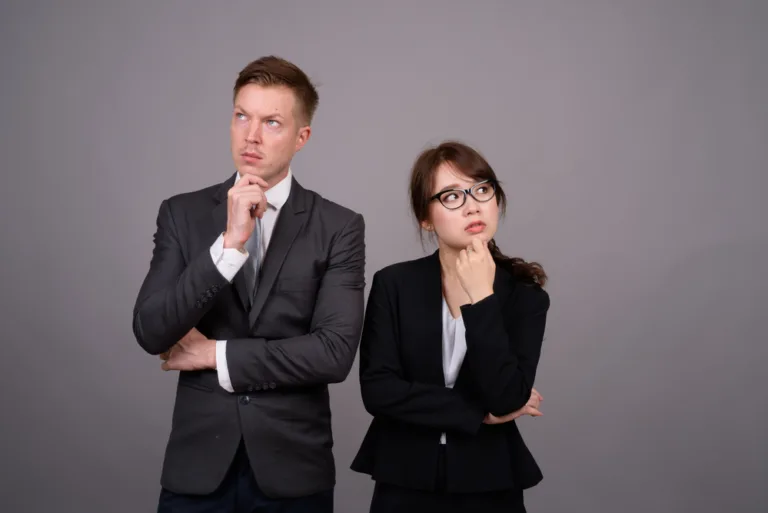 Studio shot of young handsome businessman and young beautiful Asian businesswoman wearing eyeglasses against gray background